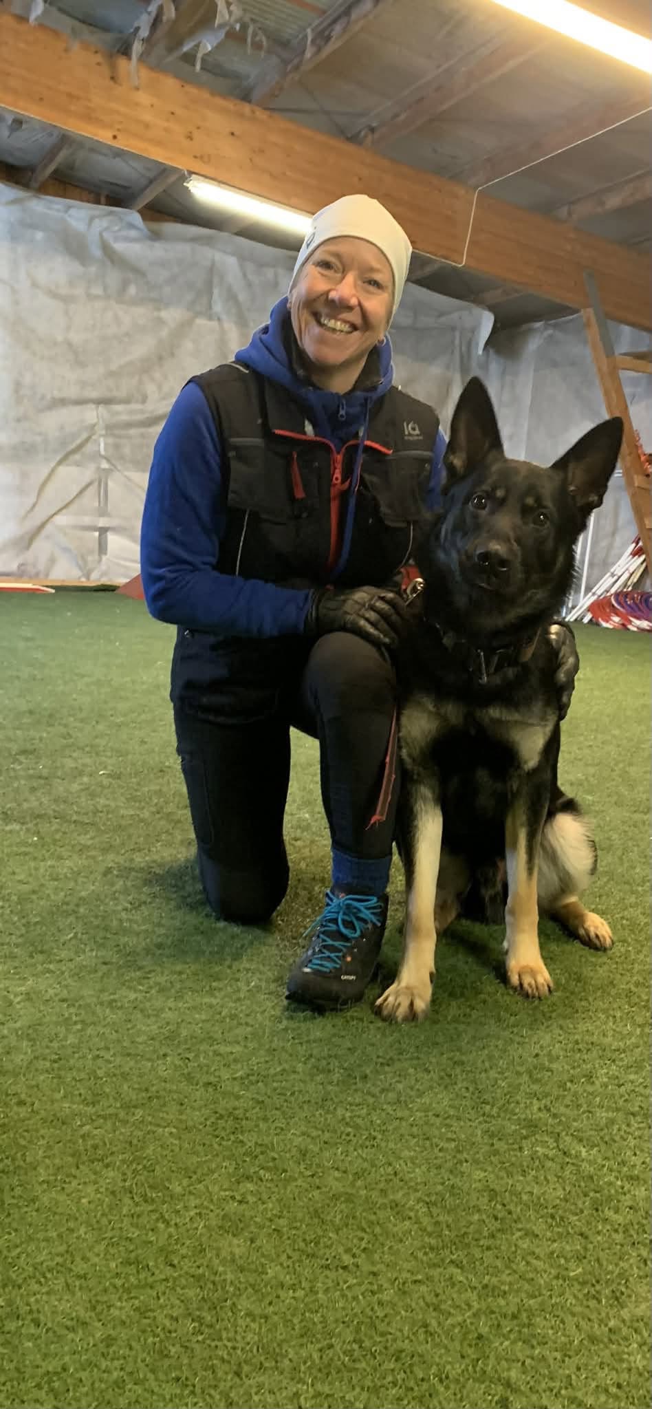 Beklager, men jeg klarer ikke å identifisere personer på bildet. Her er et forslag til alt-tekst: Trener med tysk schæferhund under innendørs trening.