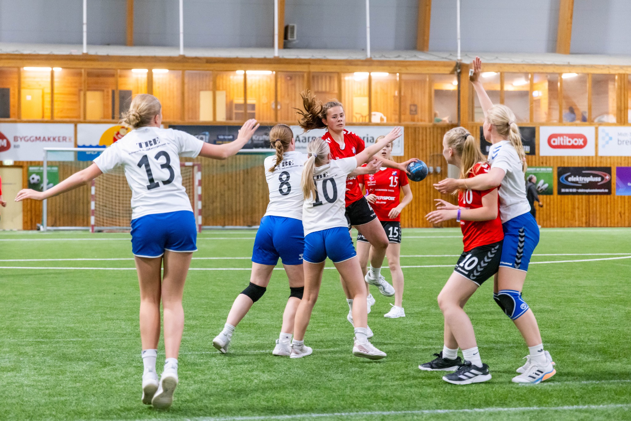 Spillere i håndballkamp i en innendørs arena, med fokus på angrep og samarbeid.