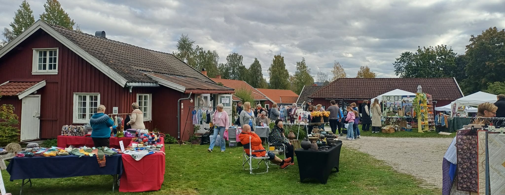 Marked med folk, boder og håndlagde varer foran en rød bygning under en skyet himmel.